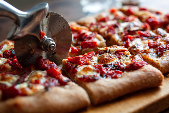 Close up of pizza cutter slicing focaccia topped with tomato sauce and garlic