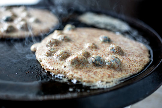 Close up of teff pancakes with chia, millet and blueberries frying on pan