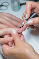 Obraz na płótnie Canvas woman hand on manicure treatment with cuticle knife in beauty salon. applying a brush on acrylic nails in the salon. vertical photo