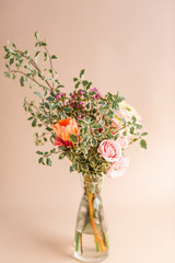 Fresh spring flowers in glass vase, peonies and roses with tan background, studio shot