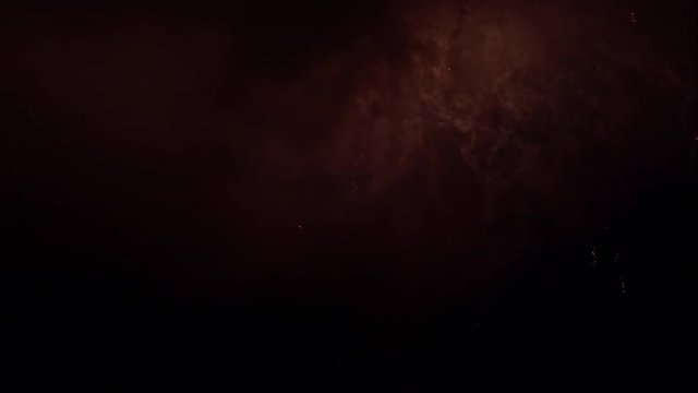 Fireworks rockets exploding in a coudy red night sky leaving white sparkling trails.