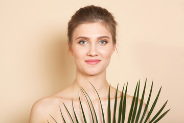 Portrait of a beautiful young girl with nude makeup and palm branches on a colored background. The...