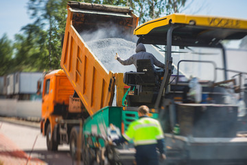 Asphalt paver machine and steam road roller during road construction and repairing works, process of asphalting and paving, workers working on the new road construction site, placing a layer