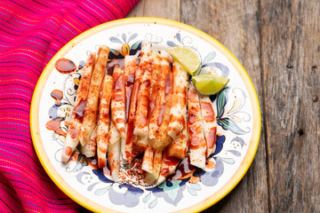 Mexican jicama  cutted with chili powder and piquant sauce on wooden background