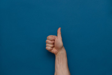 Hand clenched fist thumbs up on a blue background.