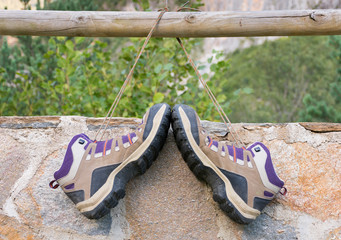 a pair of boots tied up each other and hanging on a railing by the laces and leaning on a stone wall. The hiker has put out his boots to rest his feet after hiking for a time. Horizontal photo