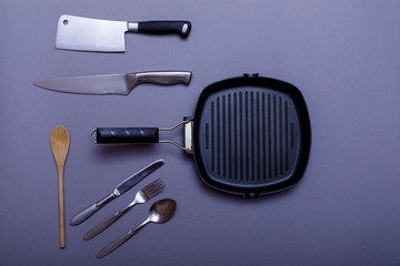 Metal knives with black on a grey table, grill pan, towel. Flat lay, layout with copy space.