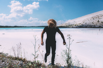 Curly blond man posing at the clear beach. Dressed all black. Awesome background, clear water and sky. Trendy, tropical and attractive man. Summer time