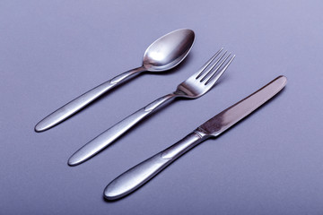 Silver fork, knife and spoon over grey background.