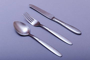 Silver fork, knife and spoon over grey background.