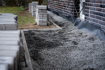 Laying gray concrete paving slabs along a house walkway. Stacks of concrete blocks are prepared to...