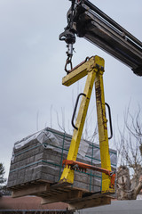 Fototapeta na wymiar Hydraulic boom truck lifting a pallet with stacks of concrete paving slabs. Gray concrete blocks for paving roads, patio, walkways or driveway.