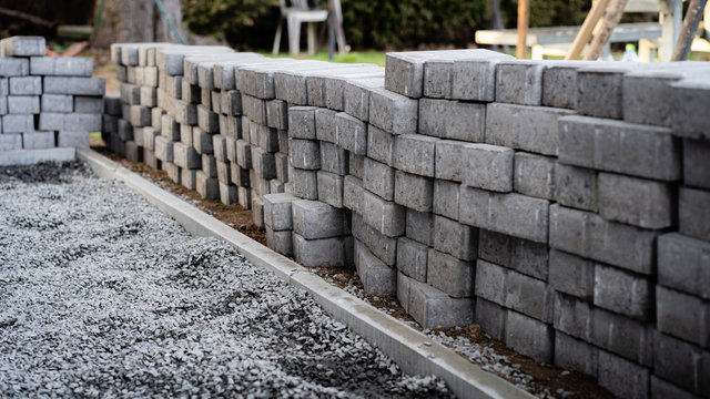 Laying gray concrete paving slabs along a house walkway. Stacks of concrete blocks are prepared to be layed on walk or patio on gravel foundation base. © hopsalka