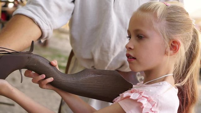 Blond child girl aims and shoots with crossbow at open air amusement park close up