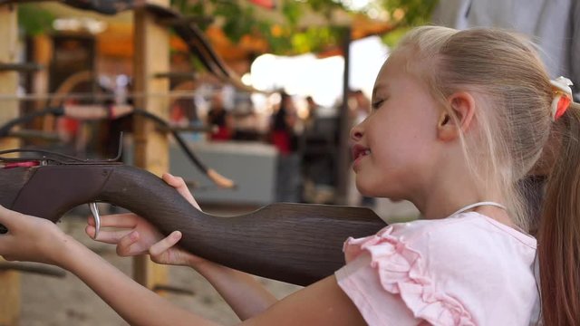 Blond child girl aims and shoots with a crossbow at open air amusement park