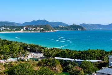 View from the hotel to clear turquoise sea, mountains, beach, jet skis, motor boats and parachutes on the coast of Dadonghai Bay in South China Sea. Sunny day