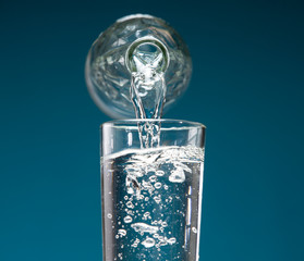 A jet of drinking water pours into a glass from a bottle