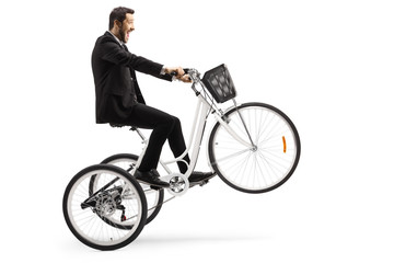 Man in a suit riding a white tricycle with front wheel up