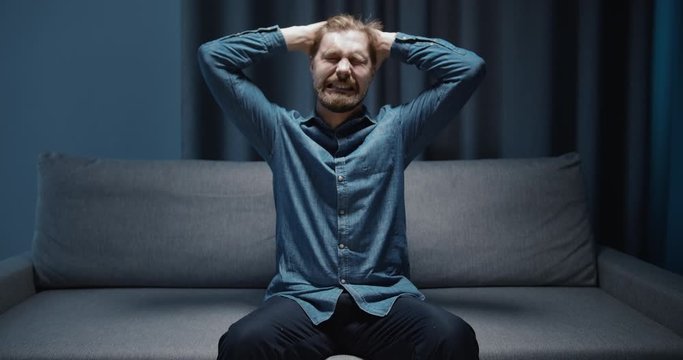 Middle-aged bearded male suffering depression, crying alone on couch, mental breakdown