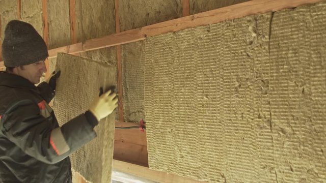 Man puts a sheet of insulation in the walls of a frame house