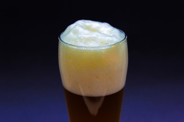 Fresh glass craft beer with white foam on top on a blue background.
