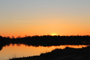 orange sunset behind the forest over the river in early spring