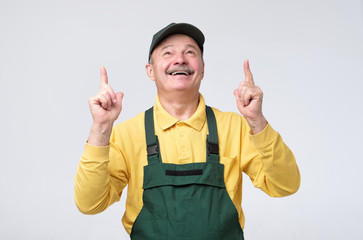 Smiling senior worker looking at camera and pointing up with index finger. Studio shot
