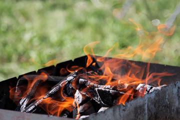 Abstract background. A bonfire in a barbecue on the background of a blurred green lawn symbolizes the opening of the barbecue season. Copy space