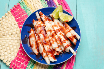 Mexican jicama  cutted with chili powder and piquant sauce on turquoise background