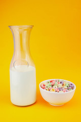 Jug of milk next to cup of fruit cereal on an orange background