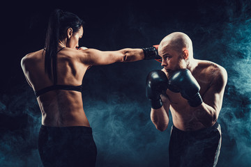 Shirtless Woman exercising with trainer at boxing and self defense lesson, studio, dark background....