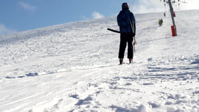 A skier silhouette in a ski suit and ski goggles slowly moving uphill on an anchor ski lift leaving traces in the snow on a cloudy blue sky background, close-up. Ski resort in the snowy mountain woods
