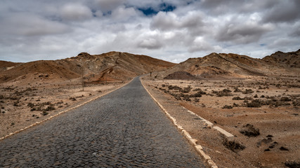 Dramatic landscape of a rocky road under the cloudy sky in the middle of the Viana desert in Boa Vista, Cape Verde