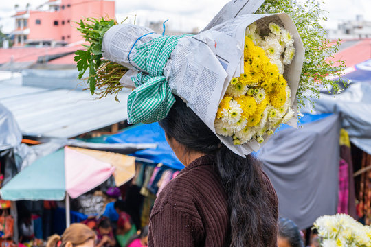 La mujer maya lleva sobre su cabeza dos ramos de flores.