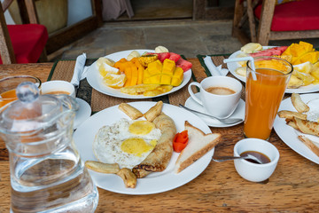 Tropical breakfast of fruit, coffee and scrambled eggs and banana pancake for two on the beach near sea. Top view, table setting.