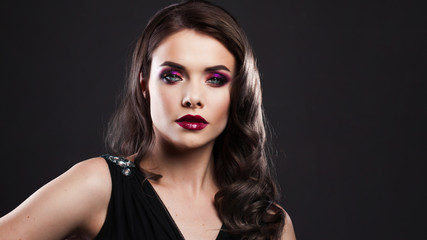 Fototapeta premium Portrait of a young luxurious woman in a low key. Bright makeup with scarlet lipstick, hairstyle with curls,