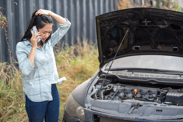A young Asian woman has a broken car in the middle of the way and must call a mechanic to fix it.