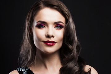 Fototapeta premium Portrait of a young luxurious woman in a low key. Bright makeup with scarlet lipstick, hairstyle with curls,