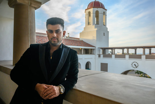 Young man in suit leans against a wall in beautiful Spanish college campus in San Diego