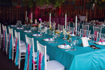 Banquet of the wedding party dinner. Luxury decor decorated tables with flowers, tableware and in turquoise pink colors. Wooden chairs with silk ribbons.