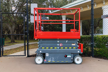 A aerial work platform also known as a hydraulic scissor lift, next to chain link fence on a tennis court 