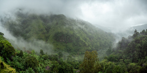 Panoramic photo of clouds flying over mountain tops and tropical rainforest in valley