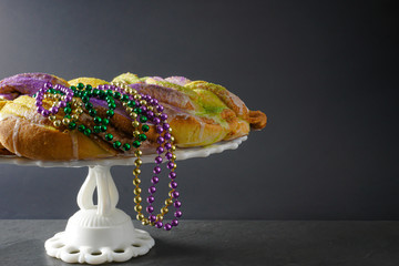 Side view of a festive Mardi Gras King Cake with green, purple, and gold beads draped over it on a...