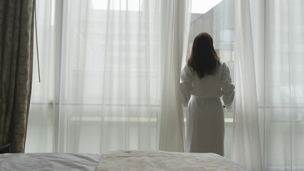 Fototapeta na wymiar Young woman in bathrobe looks from the window