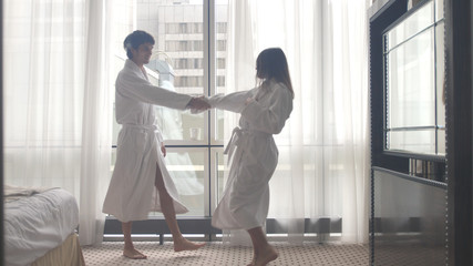Young attractive couple dancing in bathrobe after arriving to hotel.