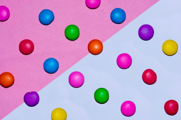 Chocolate coated candies on pink and white background