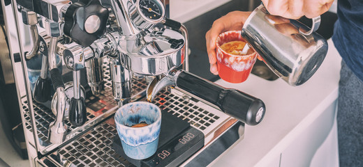 Coffee machine barista man making espresso macchiato pouring steamed froth milk in cup at home banner panoramic.