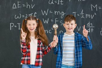 Cute little children with light bulb near blackboard at physics lesson in classroom