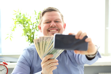 Man making self photo with mobile phone camera posing with pile of US money holding in hands