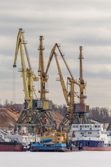 Fototapeta premium River cargo port in Moscow, Russia. Cargo ship being loaded up by a crane for loading bulk materials at port of Moscow, Russia. yellow cargo cranes in the river port. 